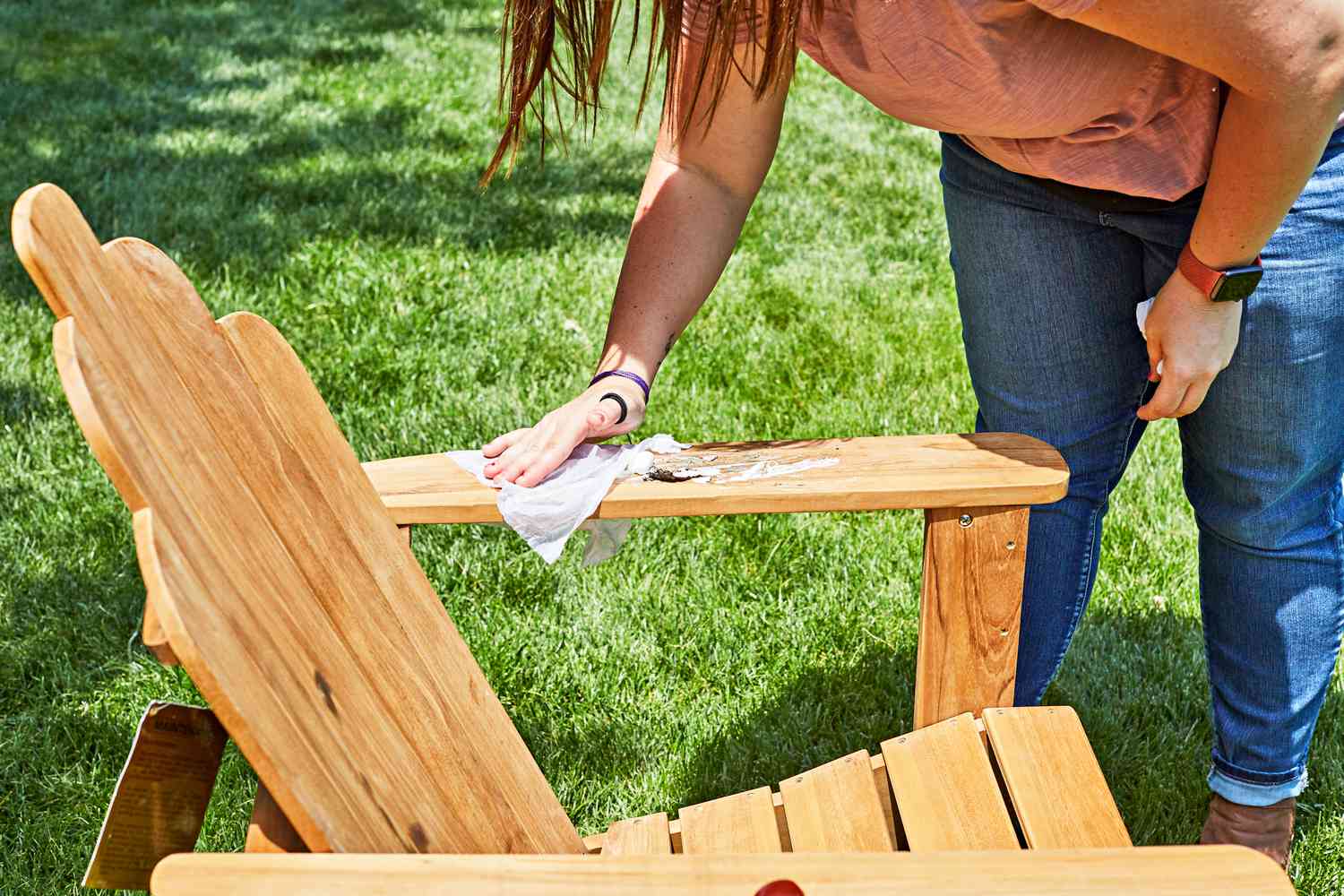 Woman wiping marshmallow from the armrest of a Grandin Road All-Natural Teak Adirondack Chair outside 