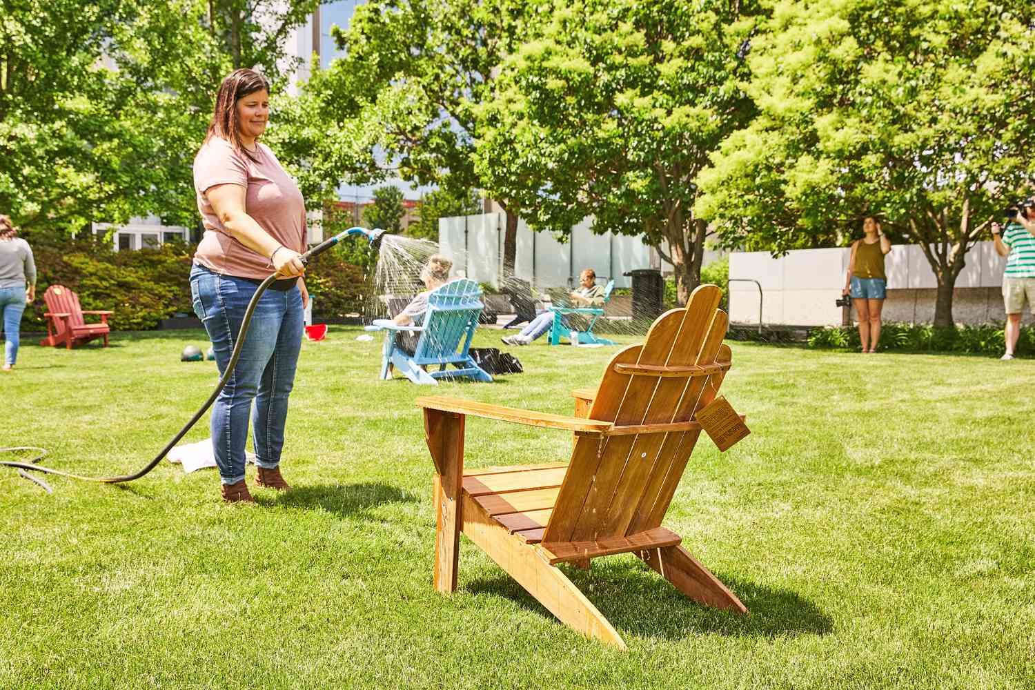 Woman spraying water on Grandin Road All-Natural Teak Adirondack Chair outside 