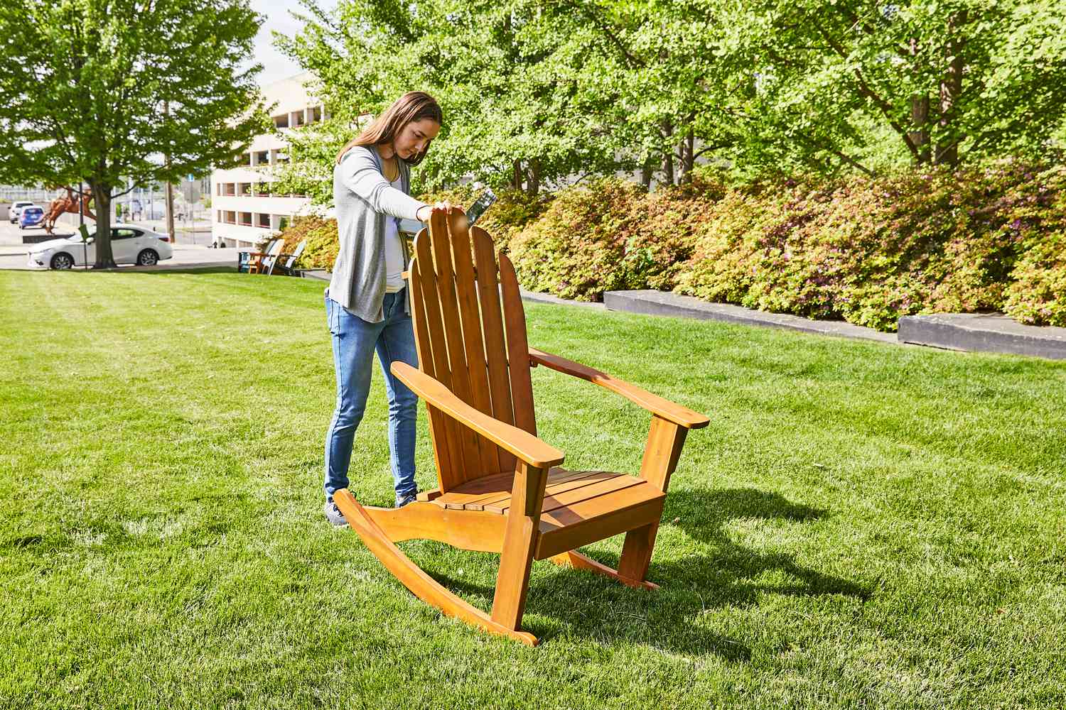 Person pushing the World Market Slatted Wood Adirondack Rocking Chair forward on a lawn