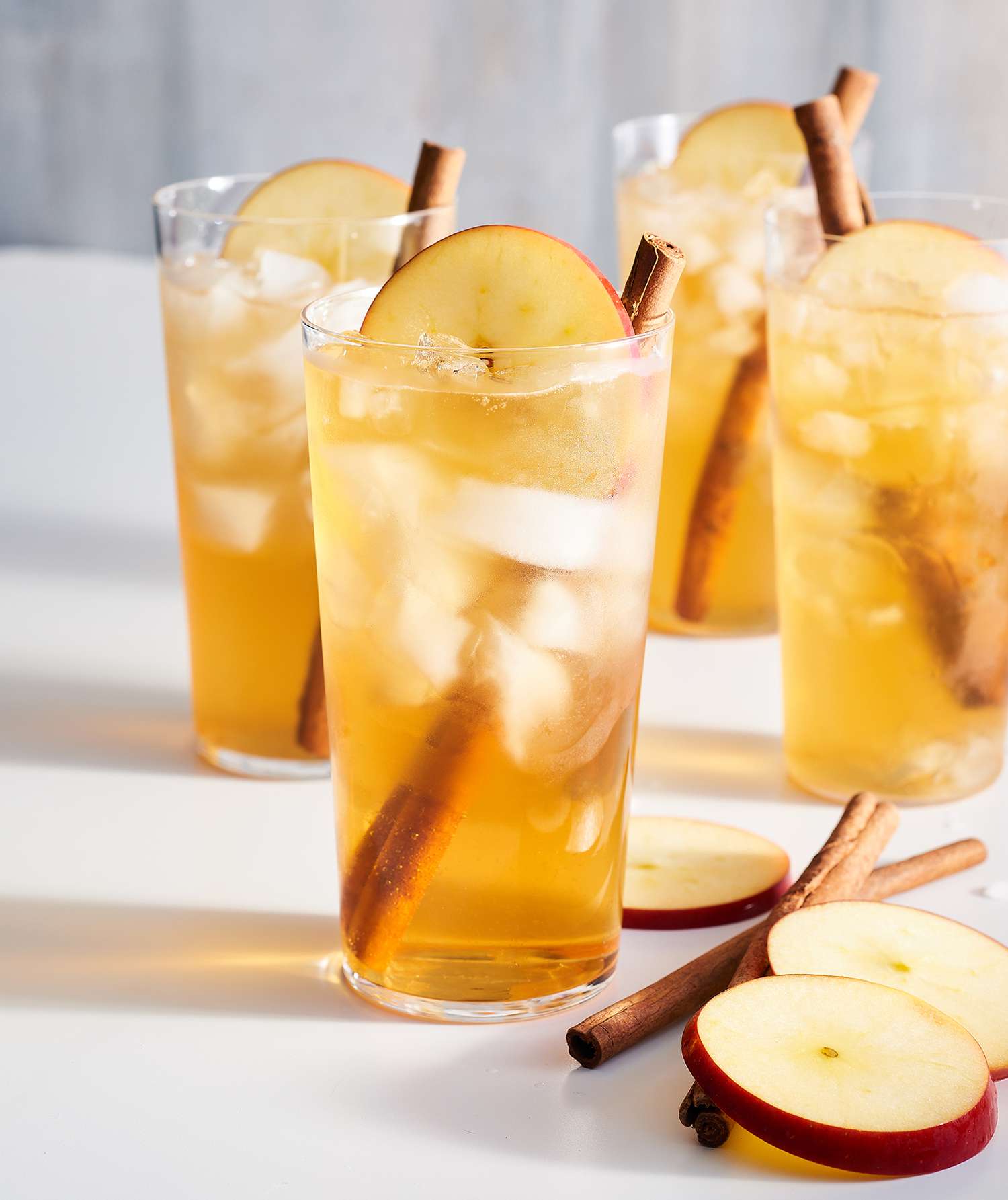 Spiced Apple Kombucha Cocktail Served in Four Tall Glasses With Cinnamon Sticks for Garnish