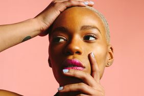 Portrait of a beautiful young woman with hands on her face and blue nails, looking sideways and isolated on pink studio background