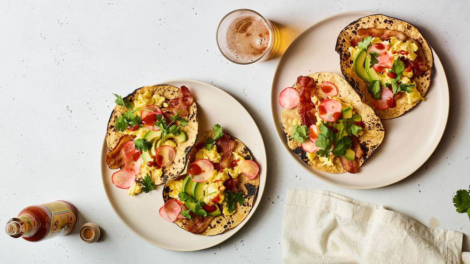 Four Crispy Bacon and Egg Tacos Served on White Plates With Hot Sauce on the Side
