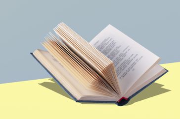 an open book lies on a yellow table, with a shadow, copy space