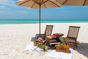 Maldives beach picnic with fruits and parasols on honeymoon sandbank with turquoise lagoon