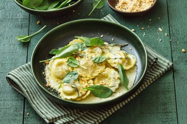 Vegan spinach, wild mushroom and walnut ravioli. Close-up composition on dark green background.