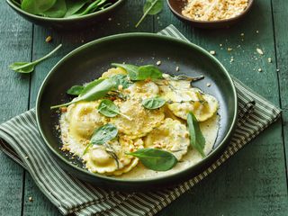 Vegan spinach, wild mushroom and walnut ravioli. Close-up composition on dark green background.