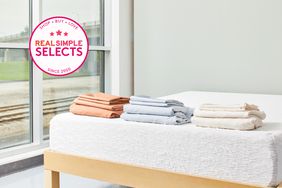 Three stacks of folded bamboo sheets on a bed with a window in the background