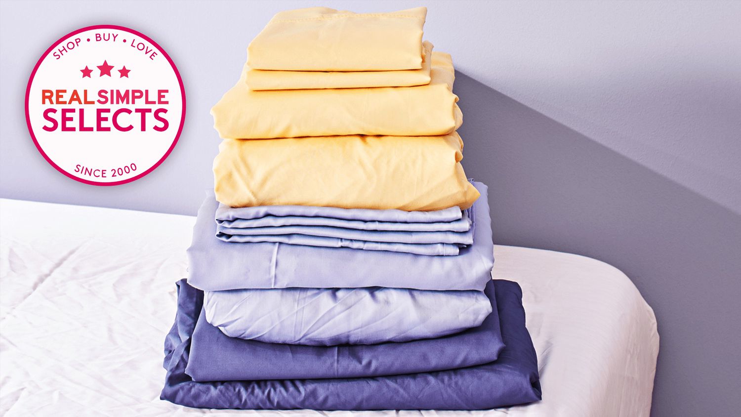 Folded yellow and blue cooling bed sheets in a stack on a bed