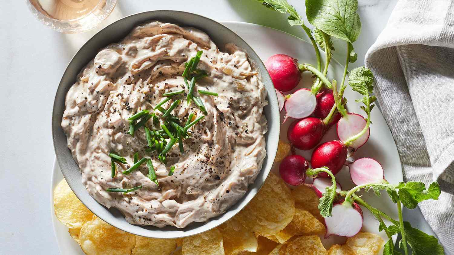 overhead view of bowl of Deeply Caramelized Onion Dip with chips and radishes