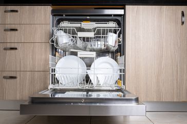 Open door of built-in dishwasher. Kitchen with integrated appliances. Plates and dishes in the dishwasher.