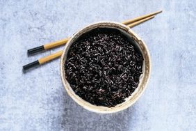 Bowl of black rice with chopsticks on blue background