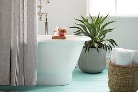 Clean Bathroom Has a White Tub With Gray Curtain, Bath Products, Woven Basket With White Towels, and Plant