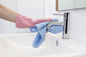 The woman, who is cleaning the faucet with microfiber cloth and gloves