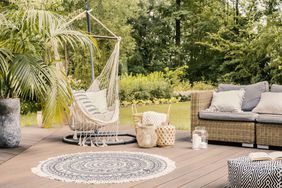 Pillows on hammock on terrace with round rug and rattan sofa in the garden.