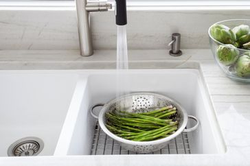 Horizontal image of fresh green asparagus and artichokes being washing in modern kitchen sink, with colander.