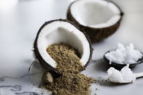 a coconut cut in half and filled with raw panela sugar, on the right side a bowl and a spoon both filled with coconut butter