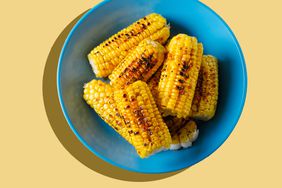 Yellow corn cobs, grilled, sprinkled with spices on a bright ceramic plate, against the background of a wooden table. The concept of cooking homemade food. Vegetarian, vegan and lean food.