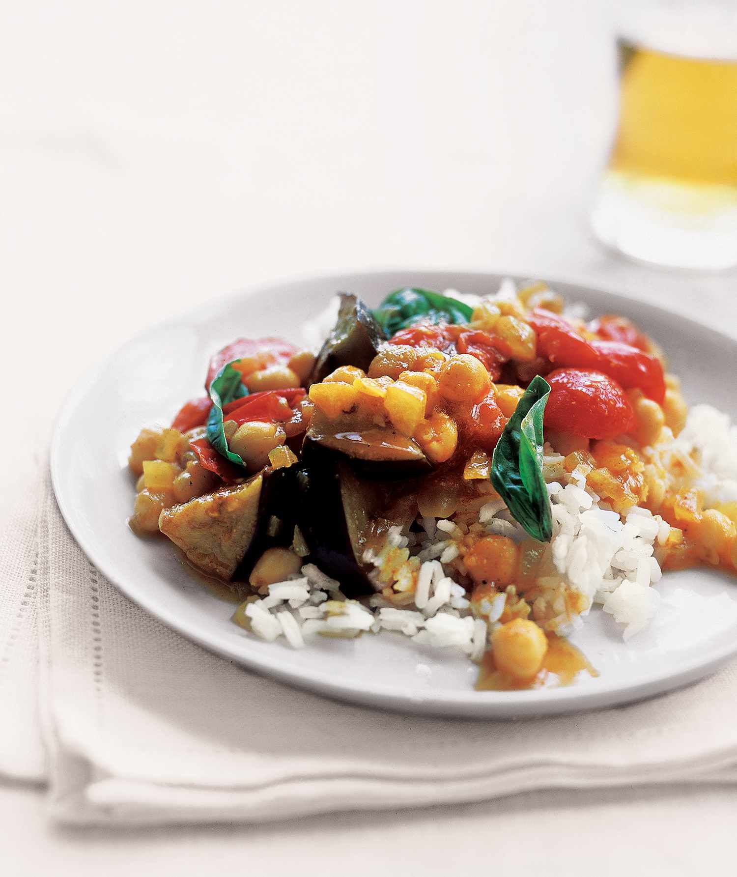 Curried Eggplant With Tomatoes, Basil, and Chickpeas, Served With White Rice on a White Plate