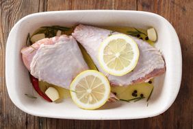 Raw turkey legs in a white casserole dish, garnished with lemon slices