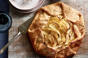 An apple galette on a rustic table with a metal serving knife and a stack of plates and forks for eating