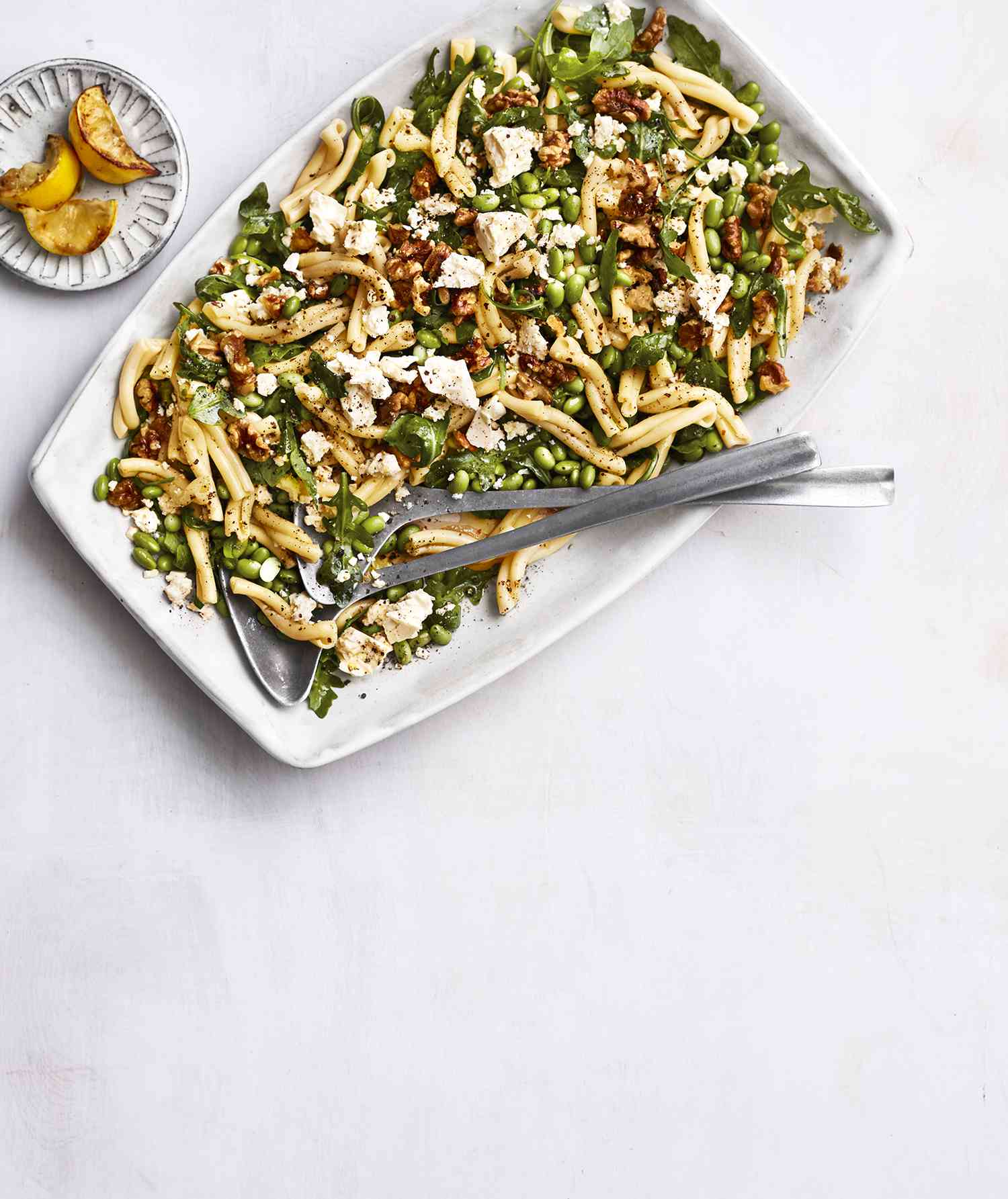 Edamame pasta salad in a serving dish displayed with roasted lemons