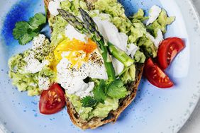 Sandwich with avocado, poached eggs, tomatoes and asparagus on a blue plate on white background