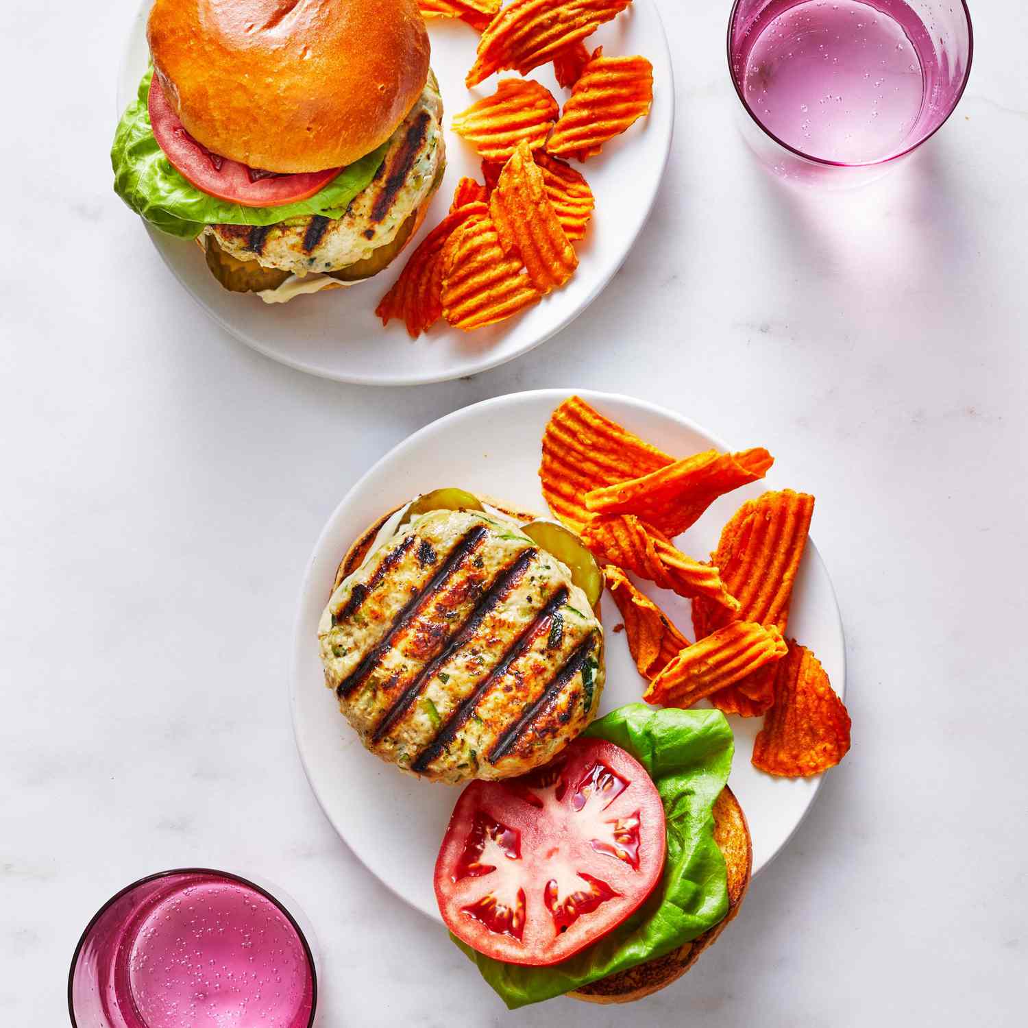 Open-face Grilled Turkey-Zucchini Burgers with chips on the side on a white plate