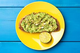 Toast with mashed avocado and pumpkin seeds on yellow plate, blue wooden planks background. Table top view. Healthy vegetarian food