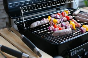 Open gas grill with shish kabobs and sausages cooking on it