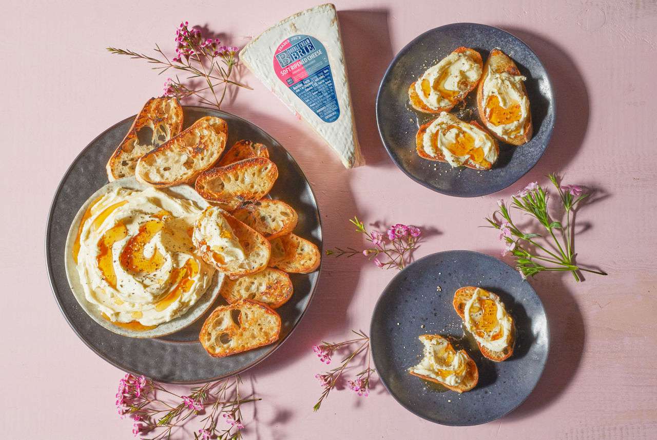 Trader Joe's Double Cream Brie; shown as recipe for Whipped Double Cream Brie; topped with Spicy Honey Sauce and cracked pepper grinds; on black plate with toasted crostini