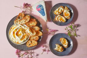 Trader Joe's Double Cream Brie; shown as recipe for Whipped Double Cream Brie; topped with Spicy Honey Sauce and cracked pepper grinds; on black plate with toasted crostini