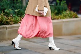  A guest wears a camel jacket, a pink bubble-skirt, white pointy boots, during London Fashion Week