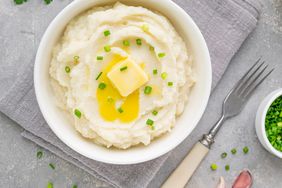 mashed potato with butter and green onions in a white bowl on a gray concrete background. Healthy food.