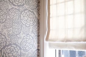 Roman shade curtain on window, next to wall with graphic floral wallpaper