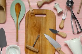 Set of different kitchen utensils on pink wooden table, flat lay