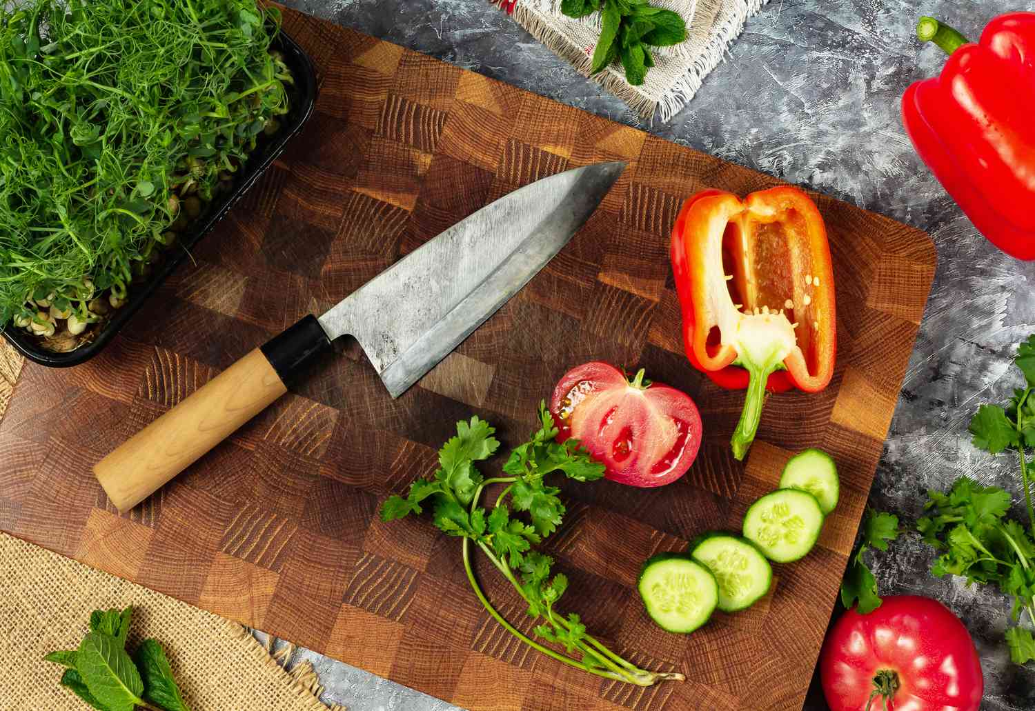 Professional Japanese knife on cutting board and fresh vegetables: tomato, bell pepper, cucumber