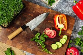 Professional Japanese knife on cutting board and fresh vegetables: tomato, bell pepper, cucumber