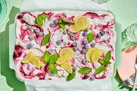 Overhead View of a Lemon-Blueberry Cake Decorated with Fresh Blueberries, Lemon Wedges, and Mint Surrounded by Small Dessert Plates and Forks