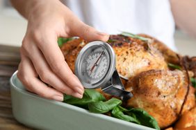 Meat temperature guide: woman measuring temperature of whole roasted turkey with meat thermometer