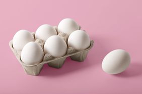 A carton of six eggs on a pink background