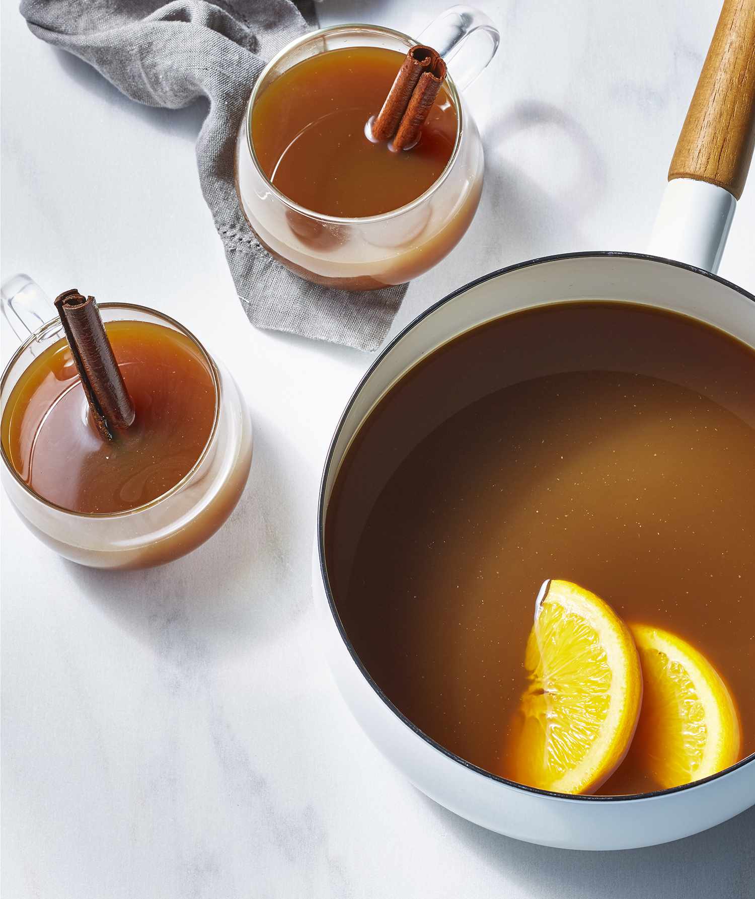 Spiked Hot Apple Cider With Molasses in a Saucepan and Served in Two Clear Cups Garnished With Cinnamon Sticks