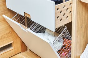 Modern wardrobe with opened metal mesh laundry basket and wooden drawers. Wooden wardrobe with flat finger pull wardrobe doors. Oak veneered plywood cabinets with light gray painted cabinet doors