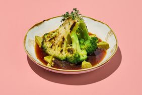 Broccoli steak in ponzu sauce on a white plate with golden trim against a pink background.