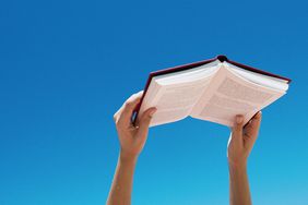 Close up of person's hands holding a book against a blue sky