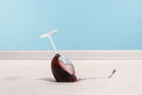 Glass of red wine spilling on white carpet with blue wall in the background