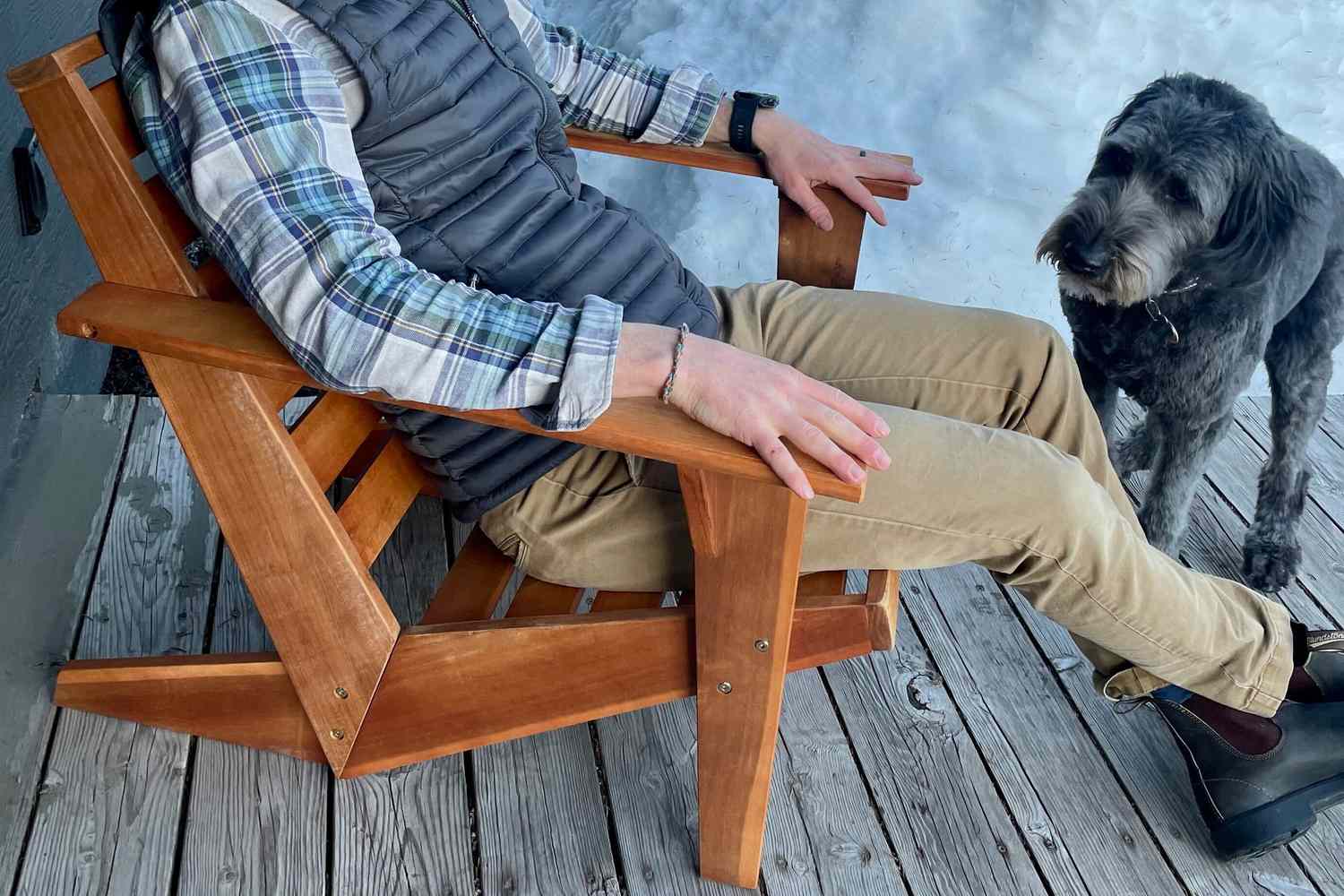 A person sitting on the Joss & Main Ursa Acacia Outdoor Adirondack Chair next to a dog