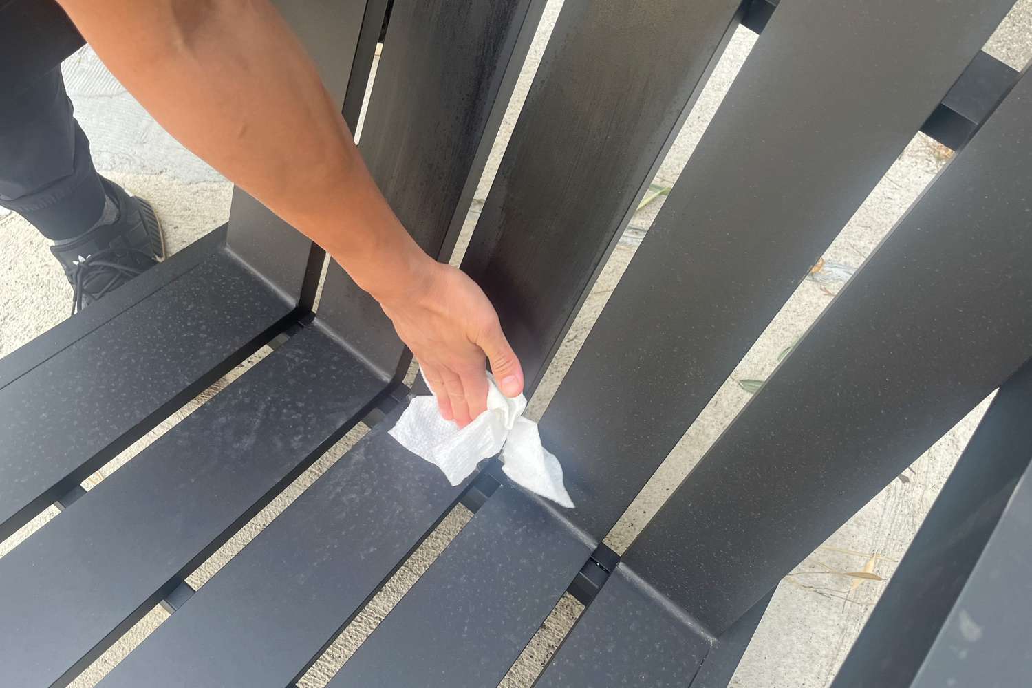 A person wiping the Pottery Barn Malibu Metal Adirondack Outdoor Lounge Chair with a paper towel