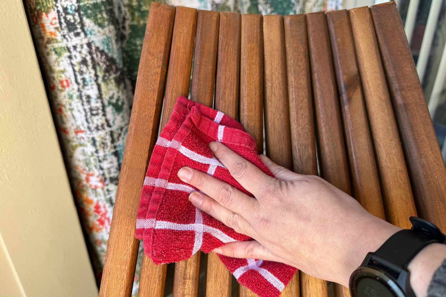 A hand using a red towel to wipe the Sand and Stable Abingdon Wood Folding Adirondack Chair