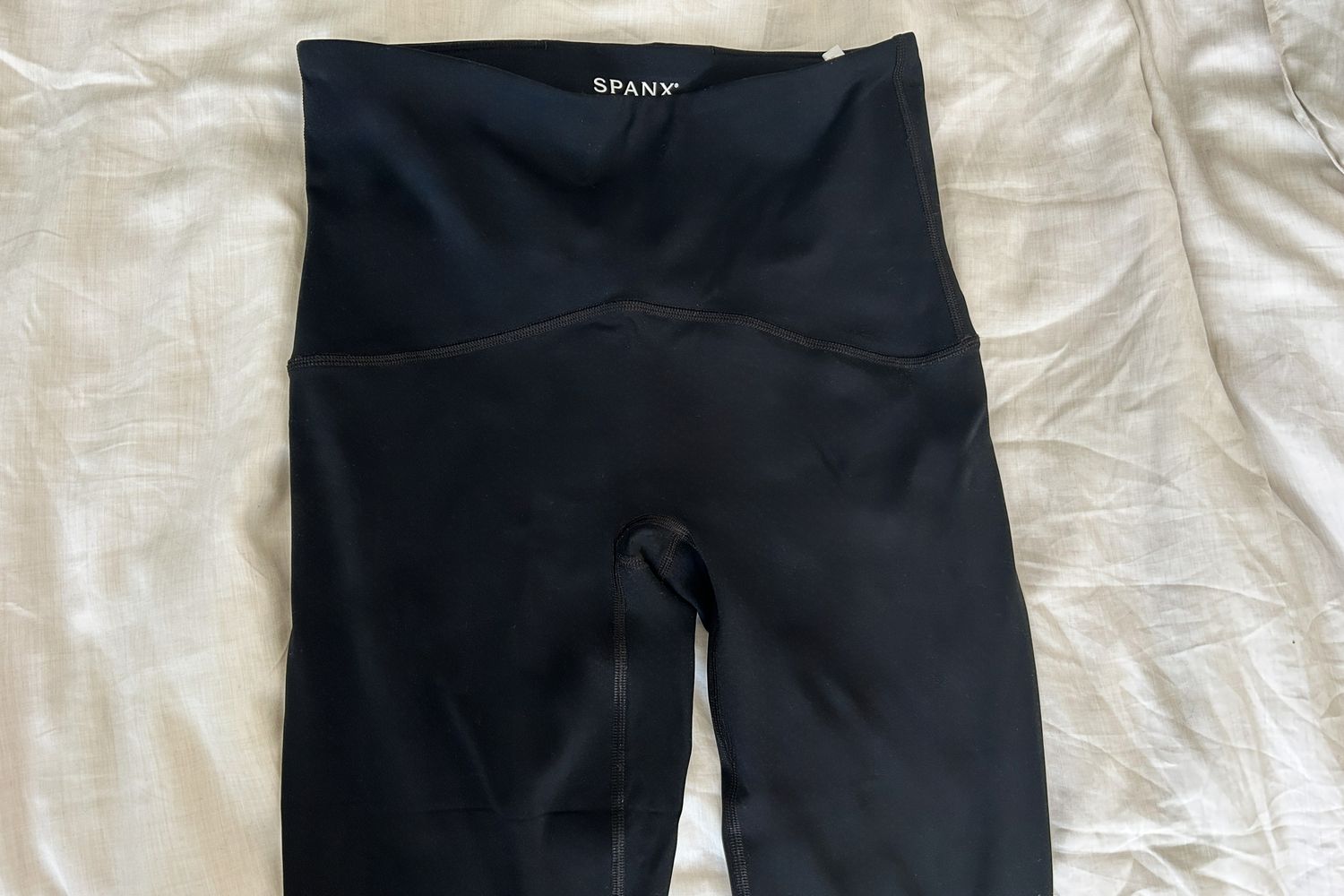 The Spanx Booty Boost Active 7/8 Leggings sit on a white comforter