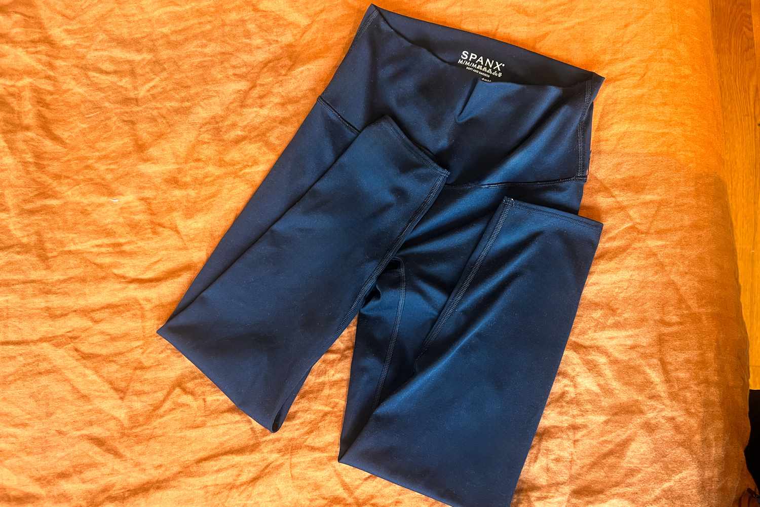 A pair of Spanx Soft & Smooth Active 7/8 Leggings folded on an orange blanket